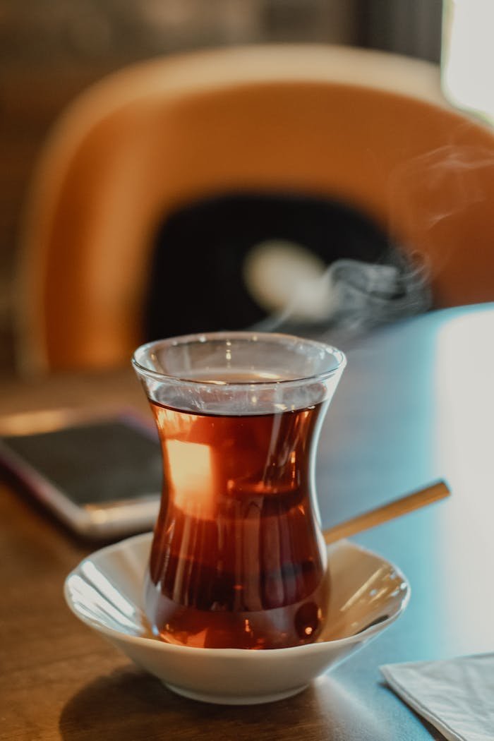 A close-up of steaming Turkish tea served in a traditional glass on a saucer, perfect for café scenes.