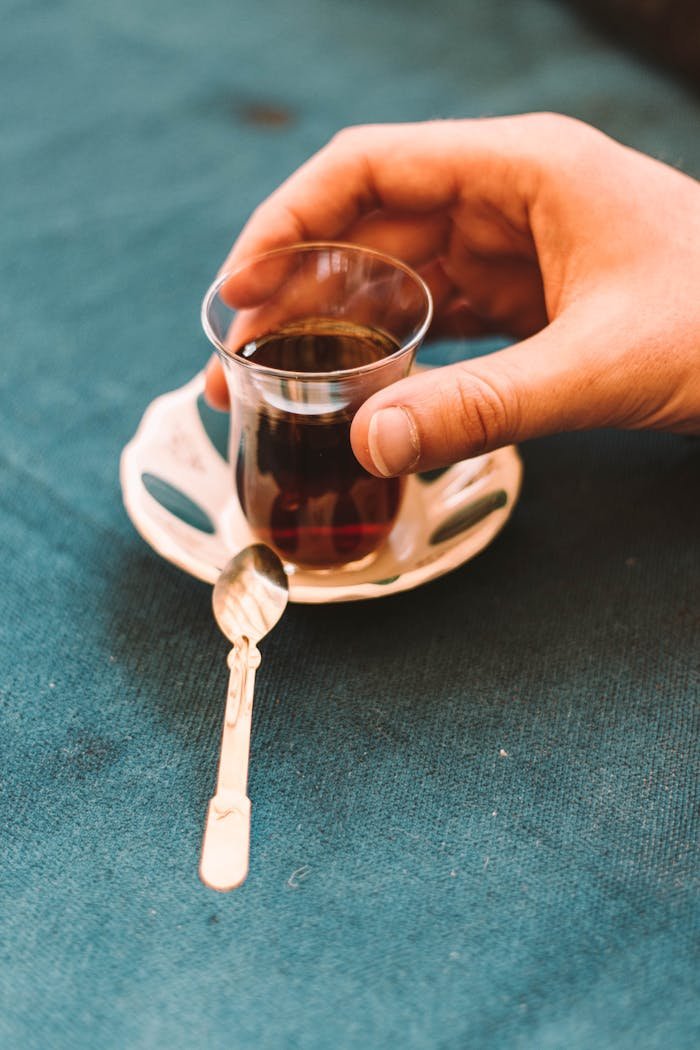 From above of crop anonymous person drinking hot tea from traditional Arabic glass placed on saucer